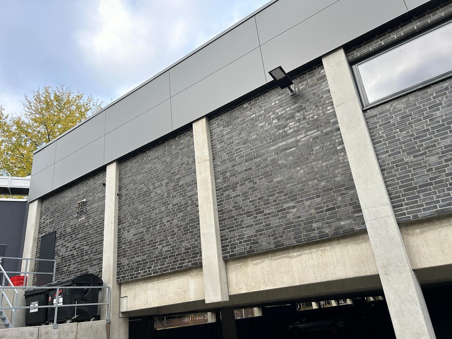 Dunkle Klinkerfassade eines Gewerbebaus mit Betonstützen über einer Tiefgarageneinfahrt